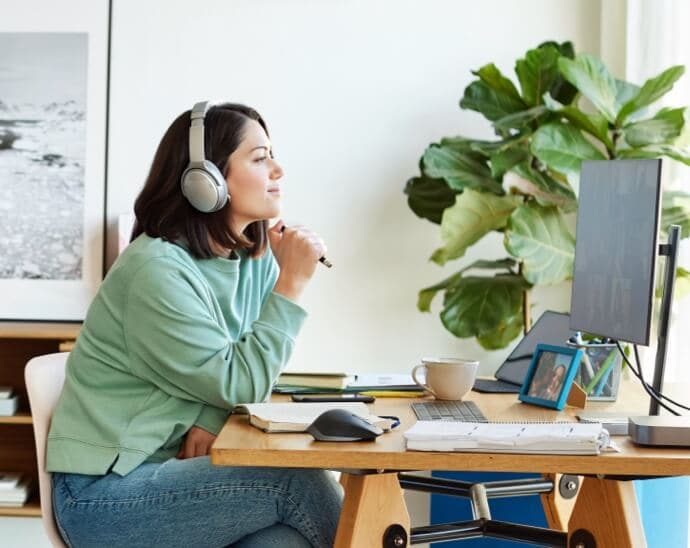 Donna con cuffie e con una penna in mano intenta a guardare il monitor di un PC