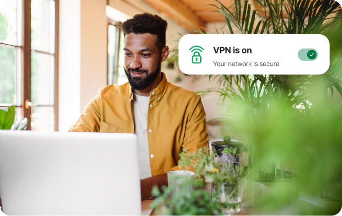 Un uomo circondato da piante guarda il suo laptop sorridendo